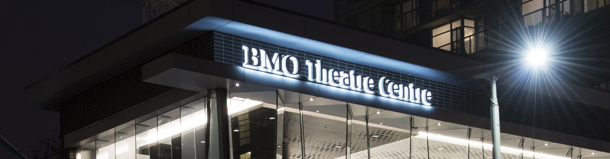 Photographed at night, the BMO Theatre Centre sign is glowing in white lights on the side of the building.