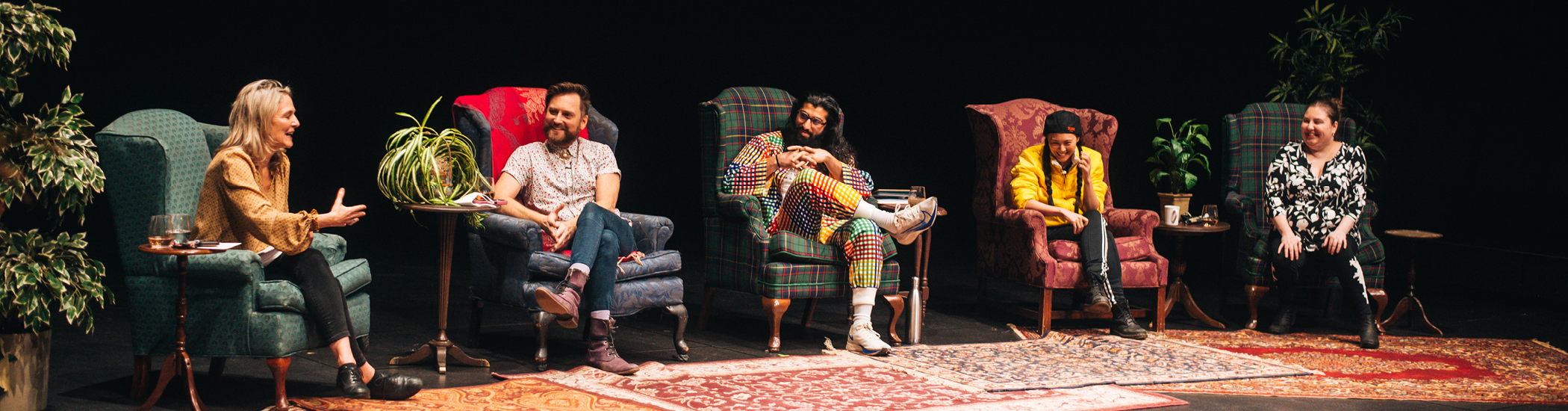 Five panelists sit onstage in armchairs of varied, colourful patterns, smiling and engaging in conversation