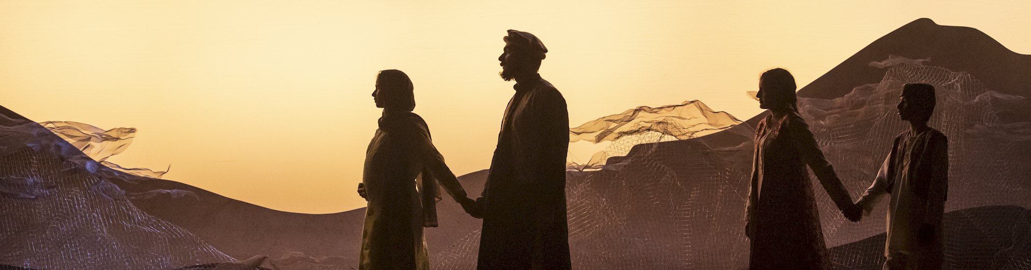 Photo of four actors walking across the stage in side profile as the sun sets behind them.