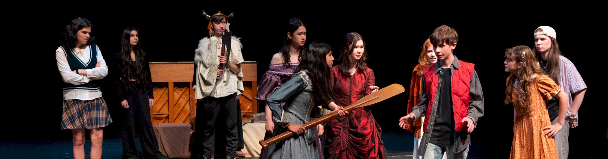 Photo of young artists in black clothing performing on a dimly lit stage.
