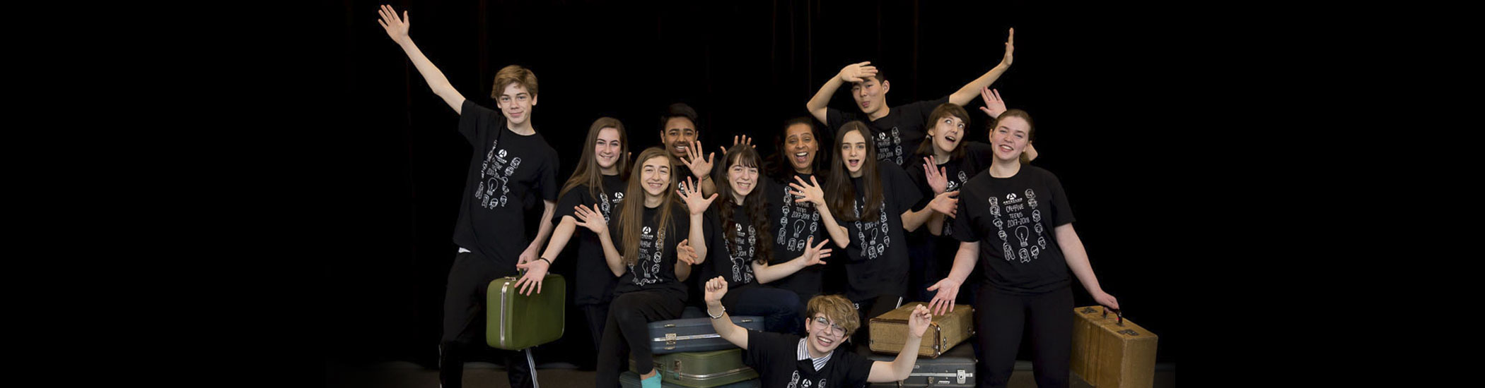 Photo of a group of teens posed around old-fashioned prop luggage and doing jazz hands.