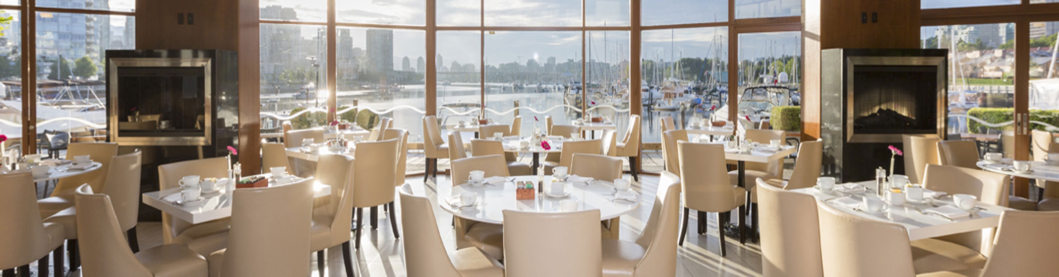 Photo of Dockside Restaurant's dining room, with large windows showcasing Vancouver views of tall buildings and the water.
