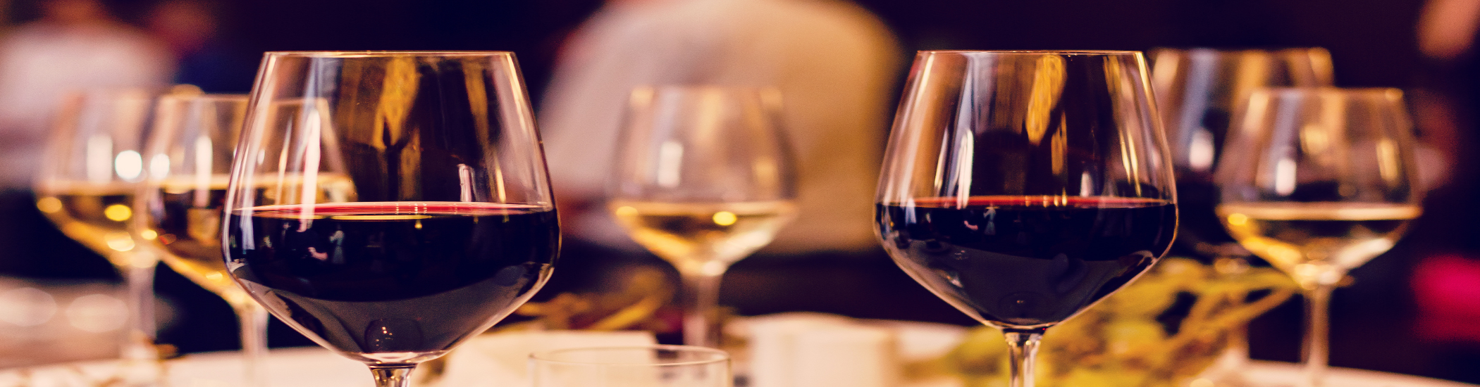 Photo of two glasses of red wine in the foreground with five glasses of white wine in the background.