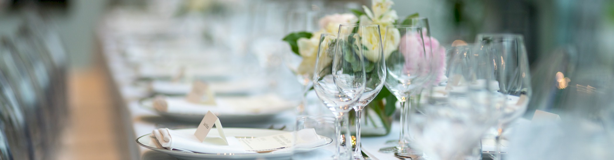A table covered with a white cloth is set with an array of glasses and flowers