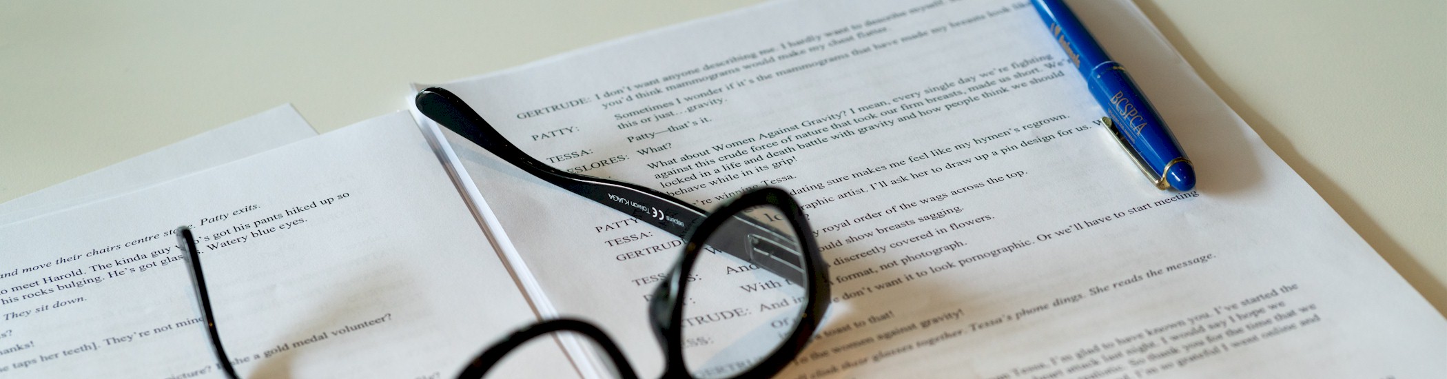 Close-up photo of an open script with a blue pen and black reading glasses sitting on top.